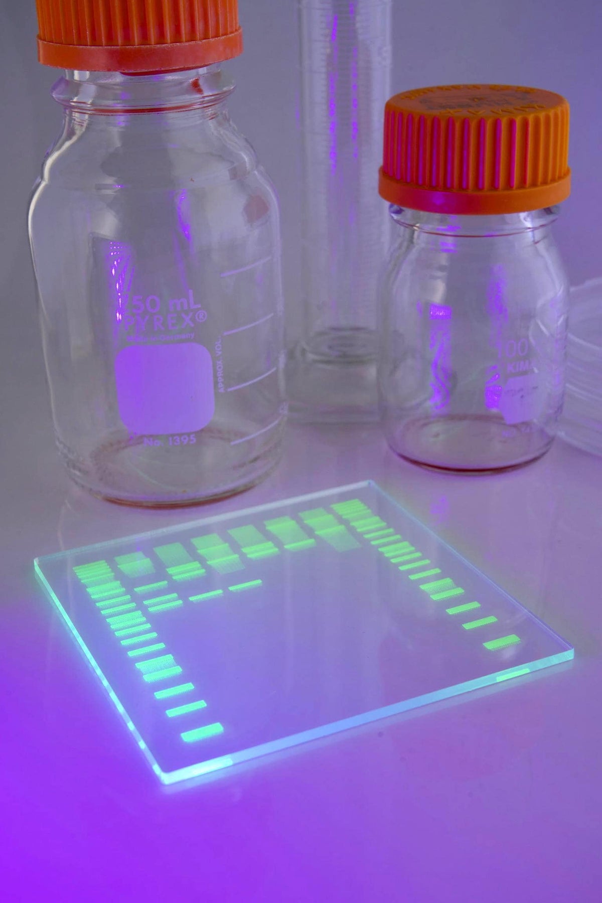 Smooth acrylic DNA gel coaster with UV green bands glowing under blacklight beside lab bottles