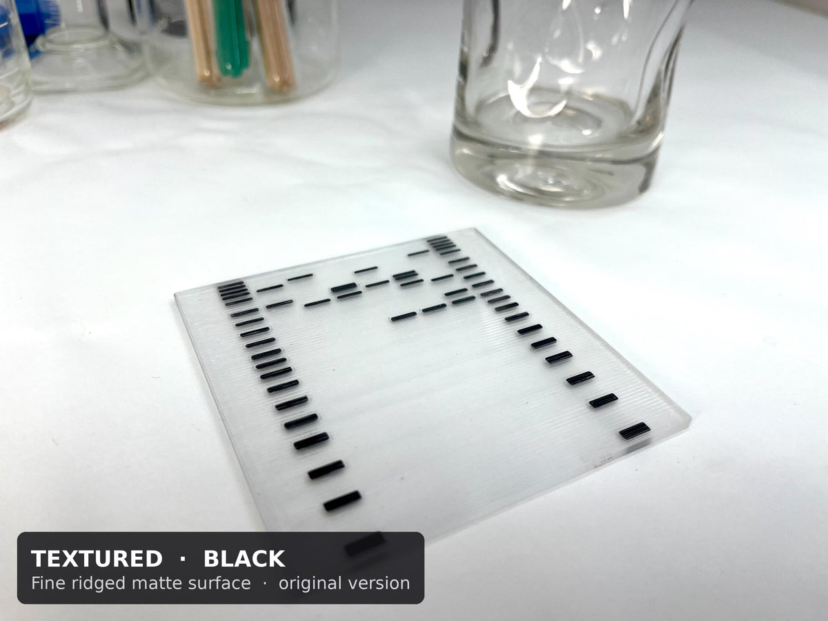Textured DNA gel coaster with black bands and a fine ridged matte surface, next to a drinking glass