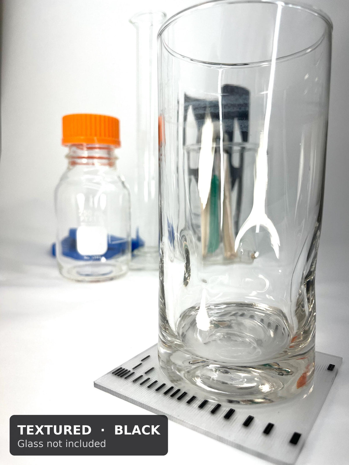 Tall glass on a textured black DNA gel coaster with a lab bottle behind (glass not included)