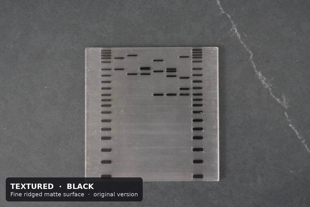 Top view of a textured DNA gel coaster showing black DNA ladder lanes on both sides and sample bands between